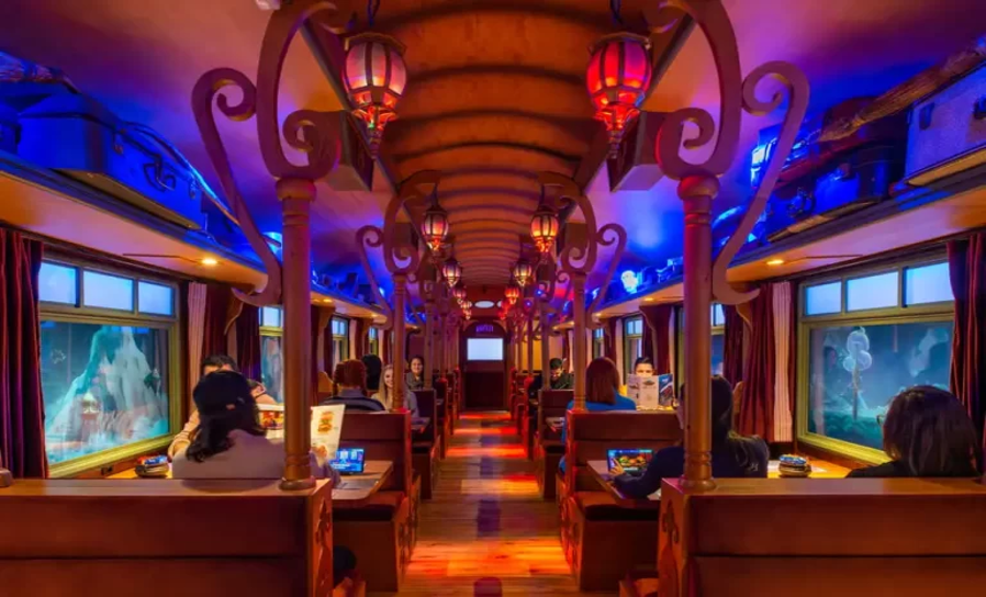 Interior do restaurante temático Hector, em Gramado, com decoração inspirada em um vagão mágico, iluminação colorida e clientes sentados às mesas.